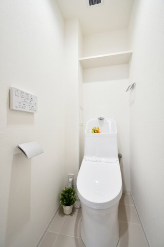 グリーンパーク大宮1号棟のトイレ|温水洗浄機能付きトイレへ新規交換済み。白を基調とした空間に、上部の棚板収納が備わり、ストック類もスマートに保管可能です。毎日使う場所だからこそ、清潔感と機能性にこだわっています。