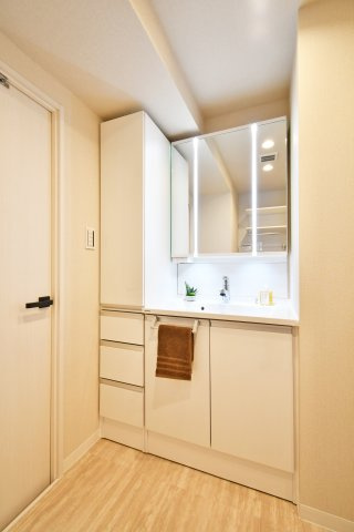 春日部ダイヤモンドマンションの独立洗面台|三面鏡タイプの洗面化粧台を新設。鏡裏収納に加え、サイドにトールキャビネットを備えているため、リネン類や小物も整理整頓が捗ります。忙しい朝の身支度をスマートに支えます。