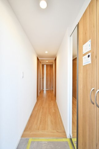ベルドゥムール春日部東の玄関|玄関扉を開けると、温もりある木目調のフローリングが奥まで続き開放感を演出。照明器具も一新され明るく家族を迎え入れる設計に。各居室へ繋がる廊下はプライバシーと動線を両立した心地よい住まいを予感させます。