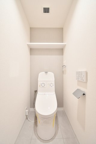 ベルドゥムール春日部東のトイレ|温水洗浄機能付きの便器へ一新された、清潔感あふれるトイレ。アクセントクロスが空間に彩りを添え、上部にはストック品の保管に便利な棚付き。毎日使う場所だからこそ、心地よさにこだわりました。