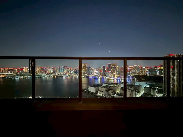 【リビングからの眺望】柵がクリアガラスになっているためリビングで座りながら空・海・街並みを一望することができます。昼と夜とで姿を変えるこの眺望を見ながら贅沢なひとときを愉しむことができます。