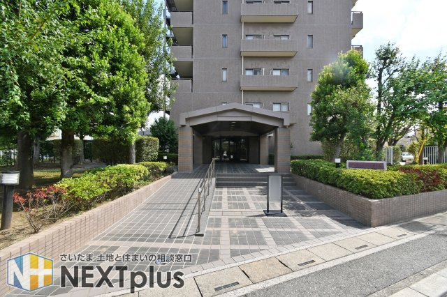 ガーデンコート大宮本郷|緑豊かな植栽に囲まれた、重厚感漂うアプローチ。スロープ付きのバリアフリー設計で、ベビーカーや車椅子での移動もスムーズです。管理の行き届いた清潔感ある空間が、居住者やゲストを優雅に迎え入れます。