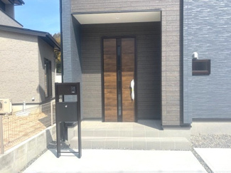 【玄関】 | 東広島市高屋町高屋東（全2区画）2号棟 | 木目調の玄関ドアがアクセントになったモダンなアプローチ。屋根のあるポーチ形状のため、雨の日の出入りや荷物が多い際にも濡れにくく快適です。