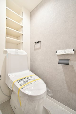 サーパス上尾第2のトイレ|温水洗浄便座付トイレを新規交換済。グレーのアクセントクロスと黒のペーパーホルダーがモダンな空間を演出します。背面の可動棚はストック収納に便利で、機能性とデザイン性を両立させました。