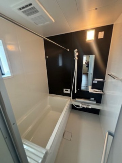 【浴室】 | 東広島市八本松飯田6丁目（全2区画）1号棟　 | ブラックのアクセントパネルが高級感を演出するシステムバス。足を伸ばしてくつろげる広さの浴槽を採用しています。横長のミラーや便利な棚など、使い勝手に配慮された設計です。