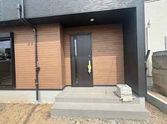 【玄関】 | 東広島市八本松飯田6丁目（全2区画）1号棟　 | 木目調の壁面が温かみを演出する玄関ポーチ。深い軒（インナーポーチ）があるため、雨の日でも濡れずに鍵を開け閉めできます。段差を抑えたタイル仕上げの階段で、スムーズな出入りをサポートします。