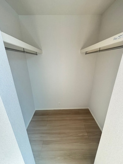 【収納】 | 安佐南区川内2丁目（全3区画）2号棟　 | 主寝室内に設けられた、ゆとりあるウォークインクローゼット。ハンガーパイプをL字型に配置し、衣類の丈に合わせて整理できます。上部の棚はバッグや帽子、寝具の予備などの保管に便利です。