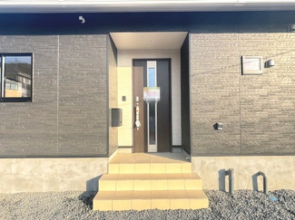 【玄関】 | 東広島市八本松飯田4丁目（全4区画）No3 | ゆとりある階段幅とフラットな玄関タイルが特徴のポーチ部分。深い軒下が雨の日の出入りをサポートします。黒の外壁と木目調ドアのコントラストが洗練された印象を与えます。