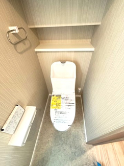 【トイレ】 | 中区江波栄町　1区画 | 温水洗浄便座付きのトイレ。背面のアクセントクロスが空間をスタイリッシュに引き締めます。ストック品の保管に便利な棚が設置されており、限られたスペースを有効に活用できる設計です。