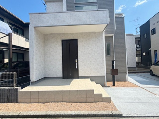 【玄関】 | グランファーレ牛野谷町3丁目　全1棟 | 広々とした玄関ポーチは屋根付きで、雨の日の出入りも安心です。機能門柱と砂利敷きの外構が整えられており、清潔感のある印象を与えます。段差の少ない階段設計で、ご家族皆様が安心して暮らせる仕様です。