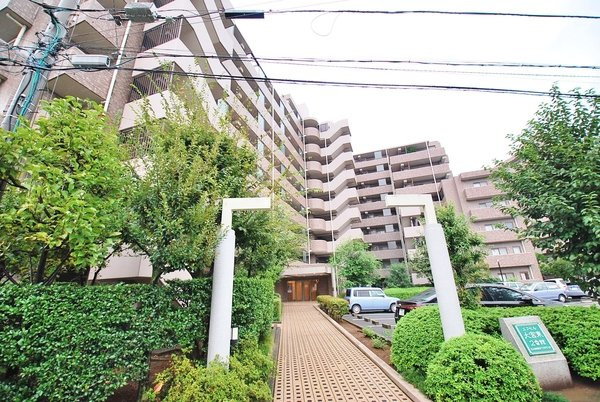 エクセル大宮東2番館のエントランス|緑豊かな植栽に囲まれた、奥行きのあるアプローチ。ベビーカーや車椅子でも安心なフラット設計が施され、住まう人を優しく迎え入れます。大規模物件ならではのゆとりと、管理の良さが伝わる空間です。