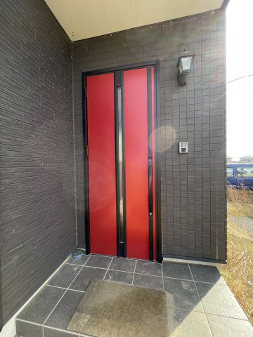 中古戸建・中古住宅　太田市新田市野井町　生品小学校・生品中学校の玄関|重厚な黒タイルの外壁に、鮮烈な赤のドアが映える。直線の美しさとコントラストを極めたモダンな玄関。