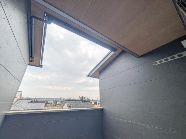 P-TELAS横田2丁目のバルコニー|バルコニーから広がる空の景色が印象的です。屋根付きで天候に影響されにくい設計となっています。壁面のシンプルなデザインが空間に落ち着きを与えています。周囲の住宅地が見渡せる開放感も魅力です。