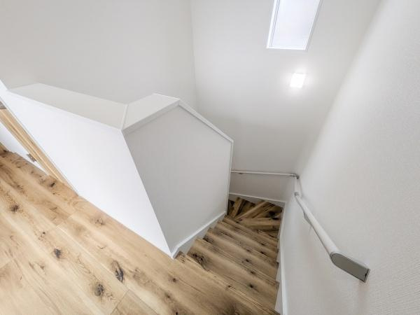 P-TELAS横田2丁目の内装|階段には手すりが設置されており安全面に配慮されています。明るい色調のフローリングが空間を広く感じさせます。壁の色合いと調和したデザインが特徴的です。採光窓から自然光が入り階段部分が明るく保たれます。