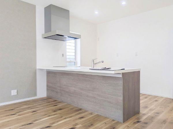 P-TELAS横田2丁目のキッチン|落ち着いた木目調のデザインが印象的なキッチンです。対面式のレイアウトが空間をゆったりと見せています。大きな換気フードと窓が設置されており採光や換気にも配慮されています。