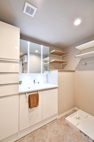 パークシティ白岡イーストガーデンの独立洗面台|三面鏡付きの洗面化粧台へ新規交換済み。洗面室には、タオルや洗剤のストックに便利な可動棚とリネン庫も付いています。明るく清潔感のある空間で、忙しい朝の身支度もスムーズに整います。