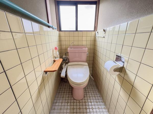 松岡　戸建てのトイレ|明るい自然光が差し込む窓付きのトイレです。壁と床のタイルが清潔感を演出しています。収納やペーパー棚も設けられています。温水洗浄便座が設置されています。小物置きスペースも便利です。