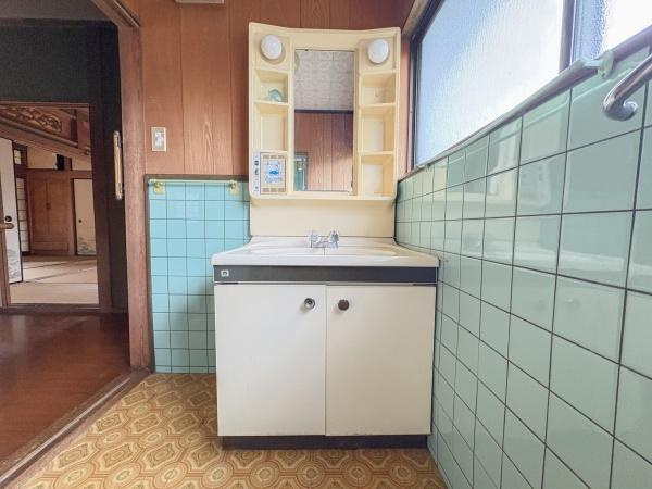 松岡　戸建ての独立洗面台|洗面台には使いやすい収納スペースが備わっています。明るい光が差し込む窓際に設置されています。清潔感を感じるタイル張りの壁が特徴です。鏡の両脇には便利な小物置きスペースがあります。