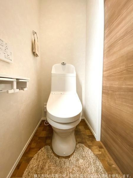 大字皆春　戸建てのトイレ|温かみのある床材とシンプルなデザインのトイレが清潔感を演出しています。壁面に設置されたペーパーホルダーやタオル掛けも使いやすい位置に配置されています。