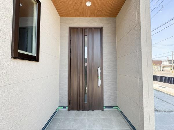 P-TELAS南津留の玄関|重厚感のある玄関ドアが印象的です。広々としたスペースで出入りがしやすいです。屋根付きで天候に左右されず落ち着いた色合いの外壁が上品です。タイル仕様の床が清潔感を演出しています。