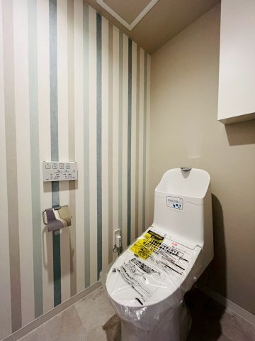 シティコーポ鴫野２号棟のトイレ|トイレは、ストライプのベージュを拾ったクロス合わせがかわいらしい空間です。
温水洗浄便座完備で快適な使い心地。