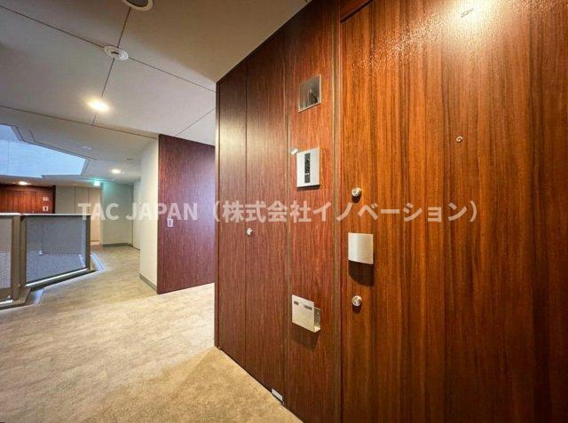 コートレジデントタワーの玄関|風雨を凌ぐ内廊下設計のプライベートアプローチ。重厚感ある木目の玄関ドアと間接照明が落ち着いた邸宅の趣を演出し、玄関を開ける瞬間まで上質さに包まれる、タワーレジデンスならではの贅沢な共用部です。