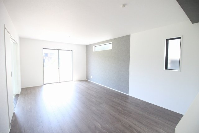 小山市駅南町5丁目　4期の居間・リビング|南側の大きな窓から明るい光が差し込む18帖のLDK。グレーのアクセントクロスと木目調の床が、落ち着きのある空間を演出します。