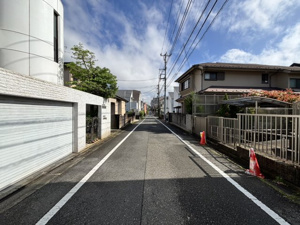 【前面道路含む現地写真】 | 高低差を活かした設計により、道路面と同等の明るい空間を確保できるのがこの土地の特長。光を遮る高い建物が周囲に少なく、開放的な空を仰ぐ暮らしが実現します。心地よい風が通り抜ける、理想の住まいを。