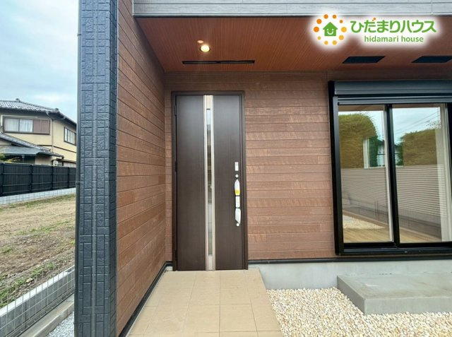 東松山市松本町1丁目　新築一戸建て　ブルーミングガーデン　01のエントランス|木目調のアクセントウォールがお出迎えする、上品で落ち着いた玄関アプローチです！屋根がしっかりせり出しているため、雨の日に傘を閉じたり、お子様をベビーカーから降ろしたりする際も濡れずに安心です♪