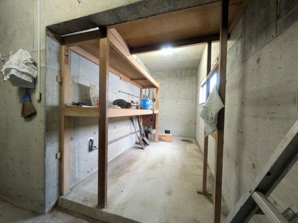 佐賀関　戸建ての内装|コンクリート壁と木製の棚が備え付けられた室内空間です。明るい照明が設置され作業スペースとして利用可能な造りになっています。窓から自然光が差し込むため日中も明るさを確保できます。