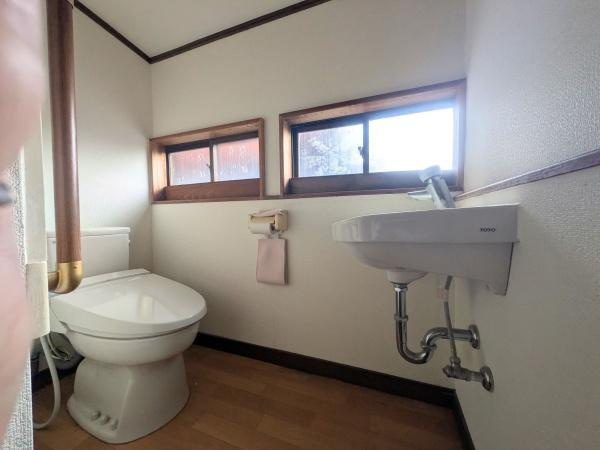 佐賀関　戸建てのトイレ|窓から自然光と自然な風が入るトイレです。手洗い器が壁付けでスペースが有効活用されています。二つの小窓が換気にも配慮されています。床の木目調が落ち着いた雰囲気を演出します。
