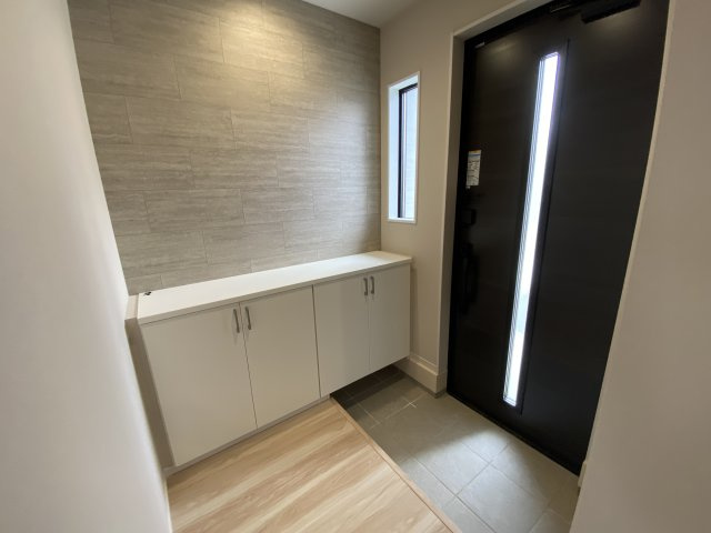 東根市羽入東【1号棟】の玄関|落ち着いた色調のアクセントウォールが、高級感漂う玄関を演出。横長で使い勝手の良いシューズボックスは、飾り棚としても活用でき、空間に彩りを添えます。