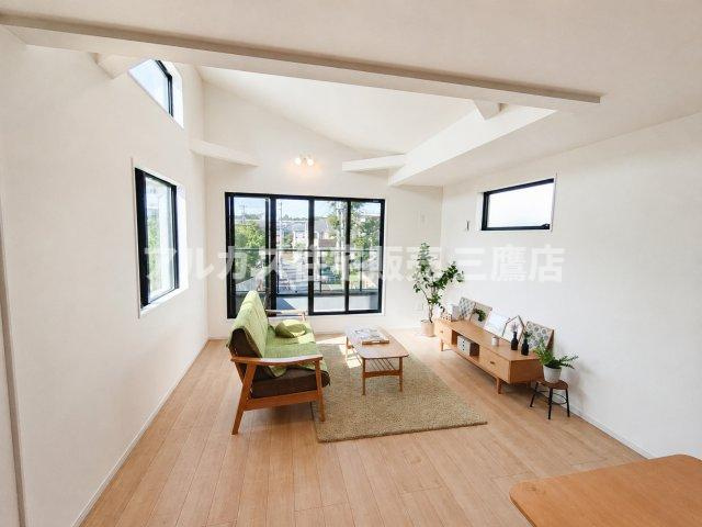 府中市幸町1丁目　京王線　府中駅　新築戸建の居間・リビング|高窓からの採光と解放感のある勾配天井が印象的なリビング。落ち着いたグリーンのソファとナチュラルテイストの家具が調和しています。