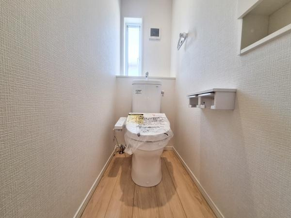 里第3-2号棟のトイレ|シンプルな内装が特徴のトイレです。小窓から光が入り空間が明るく感じられます。床の色合いがナチュラルで清潔感があります。壁面収納やペーパーホルダーが設置されています。空間がすっきりとした印象です。