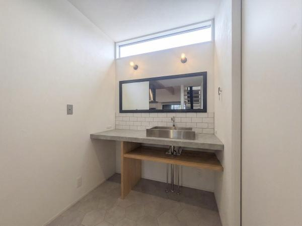 久原南2丁目　戸建て(美容室併設)の独立洗面台|モルタル調カウンター×タイルの造作洗面台。
ステンレスのスクエアシンク、黒フレームミラー、ブラケット照明が上質な空間を演出。
高窓から差し込む自然光も心地よい一室です