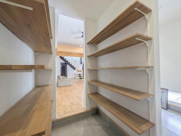 久原南2丁目　戸建て(美容室併設)の玄関|玄関には壁面を活用した可動式の棚が備え付けられており空間を有効に利用できます。木目調の棚板が空間に温かみをプラスしています。土間仕上げで汚れに強くお手入れも簡単です。