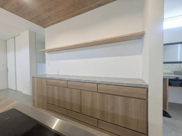 久原南2丁目　戸建て(美容室併設)のキッチン|キッチン背面には、木目調の扉とモルタル調カウンタートップが美しい造作収納を設置。
たっぷりの収納量と上部の飾り棚で、すっきりとした空間を保ちながらインテリアとしても映える仕上がりです。