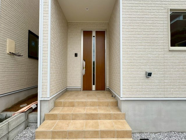 「利便性MAX」高知市南金田第1　2号棟新築一戸建ての玄関|温かみのある木目調の玄関ドアが映えるアプローチ。屋根付きのポーチ仕様で、雨の日の出入りもスムーズです。