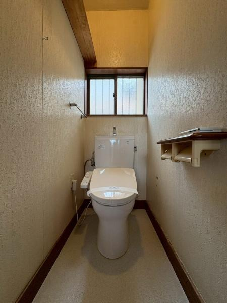 鎌倉市植木の中古一戸建のトイレ|窓が設けられており採光と換気がしやすいトイレです。ペーパーホルダーや収納棚も配置されています。温水洗浄便座を備えた仕様です。落ち着いたカラーの内装が特徴です。無駄のないシンプルな空間です。