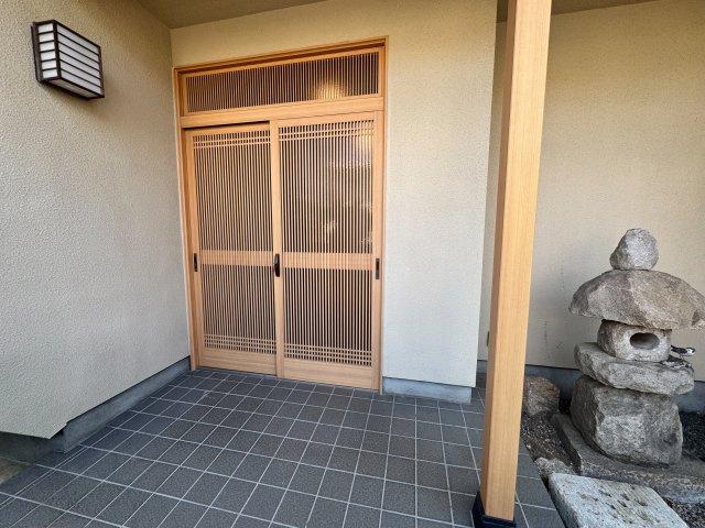 入間市東町7丁目中古戸建の玄関|美しい格子戸が主役の和風玄関です。木の温もりを活かした落ち着きある佇まいで、ピカピカした派手さを抑えた上質な質感が魅力。灯篭を添えた坪庭風の演出が、毎日の帰宅時に心癒やす贅沢な空間を創り出します。