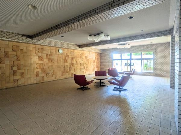 アーバン田室第二期棟のエントランス|広々としたエントランスが印象的です。タイル張りの床と大きな窓から差し込む自然光が開放感を演出しています。複数の椅子やテーブルが設置されておりゆったりとした空間が広がっています。