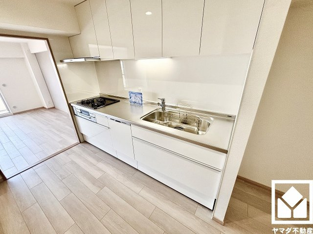 グランドヒル西宮高座台マンションＡ棟のキッチン|明るい白色で統一された清潔感のあるデザインが魅力のシステムキッチンです。リビングだけでなく、洗面室へも出入りできる2WAYキッチンとなっています。風通しが良く、家事動線にも配慮された設計です。