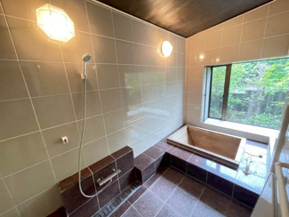 【浴室】 | あすみが丘〈圧巻の199坪〉中古戸建　JR「土気」駅 | 木の温もりに癒やされる浴槽と木目調の天井が、高級旅館のような風情を醸し出すバスルームです。品のあるタイル壁や落ち着いた床面、お洒落な照明が上質な空間を演出。大きな窓からは庭の緑を楽しめます。