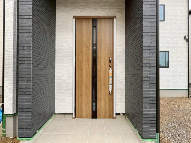 「広々インナーバルコニー」高知市東城山町2号棟　新築一戸建ての玄関|黒のアクセント壁と木目調ドアが調和した、モダンで重厚感のある外観。
