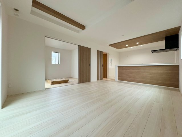 「独立洗面設計」高知市東城山町1号棟　新築一戸建ての居間・リビング|キッチンや天井の木目が映えるモダンな空間。隣の洋室を開放して広く使えます。