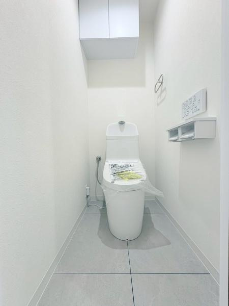 クリオ大師公園南壱番館のトイレ|シンプルなデザインのトイレで手入れのしやすさが感じられます。壁付け収納が設置されており実用性も考慮されています。ペーパーホルダーやリモコン操作パネルがコンパクトにまとめられています。