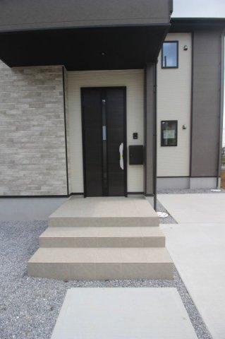 小山市東城南２丁目の新築一戸建の玄関|ブラックの玄関ドアと石目調の外壁が調和した玄関ポーチ。建物の内側に入った配置で、雨が直接吹き込みにくい設計です。