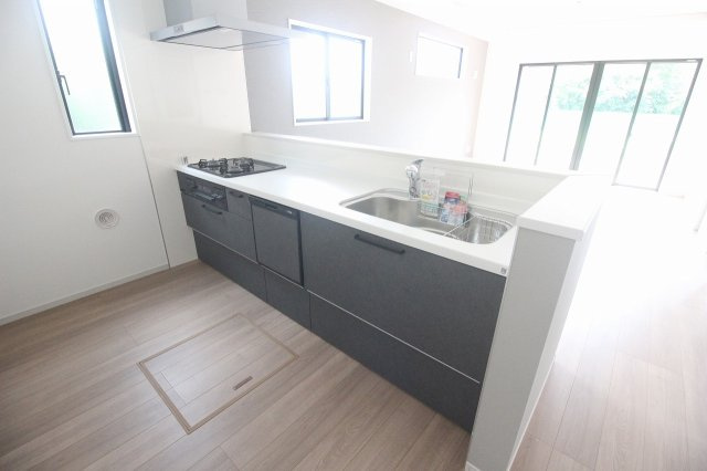 小山市東城南２丁目の新築一戸建のキッチン|落ち着いたグレーの対面式キッチン。3口コンロと食器洗浄乾燥機を備え、床下収納には使用頻度の低い調理器具や備蓄品をしまえます。