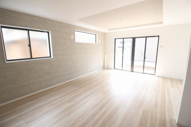 小山市東城南２丁目の新築一戸建の居間・リビング|グレーのアクセントクロスや折上天井が空間に奥行きを演出。大きな掃き出し窓から屋外へ出入りでき、室内に光を取り込みます。