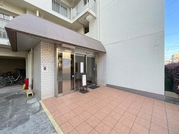 カサベルダのエントランス|広々としたタイル貼りのエントランスが印象的です。屋根付きで雨の日も快適に出入りできます。ガラス扉が開放的な雰囲気を演出しています。バリアフリーに配慮した設計もうかがえます。